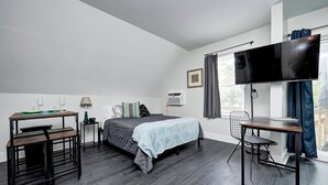 Un dormitorio moderno con cama, escritorio, silla, televisor y ventana con cortinas.