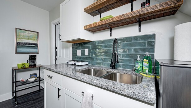 Una cocina moderna con encimeras de granito, un lavamanos de acero inoxidable y repisas de madera sobre la encimera.