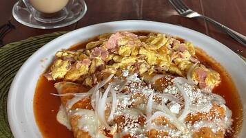 A plate of enchiladas topped with cheese, onions, and a red sauce, served with a glass of iced coffee on a wooden table.