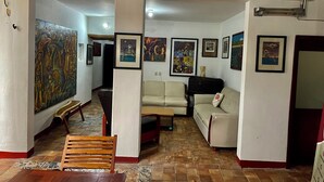 A living room with a sofa, a wooden chair, a table, and a large painting on the wall. - HOTEL CASA TERESA GALERIA CAFE  (Juchitan de Zaragoza)