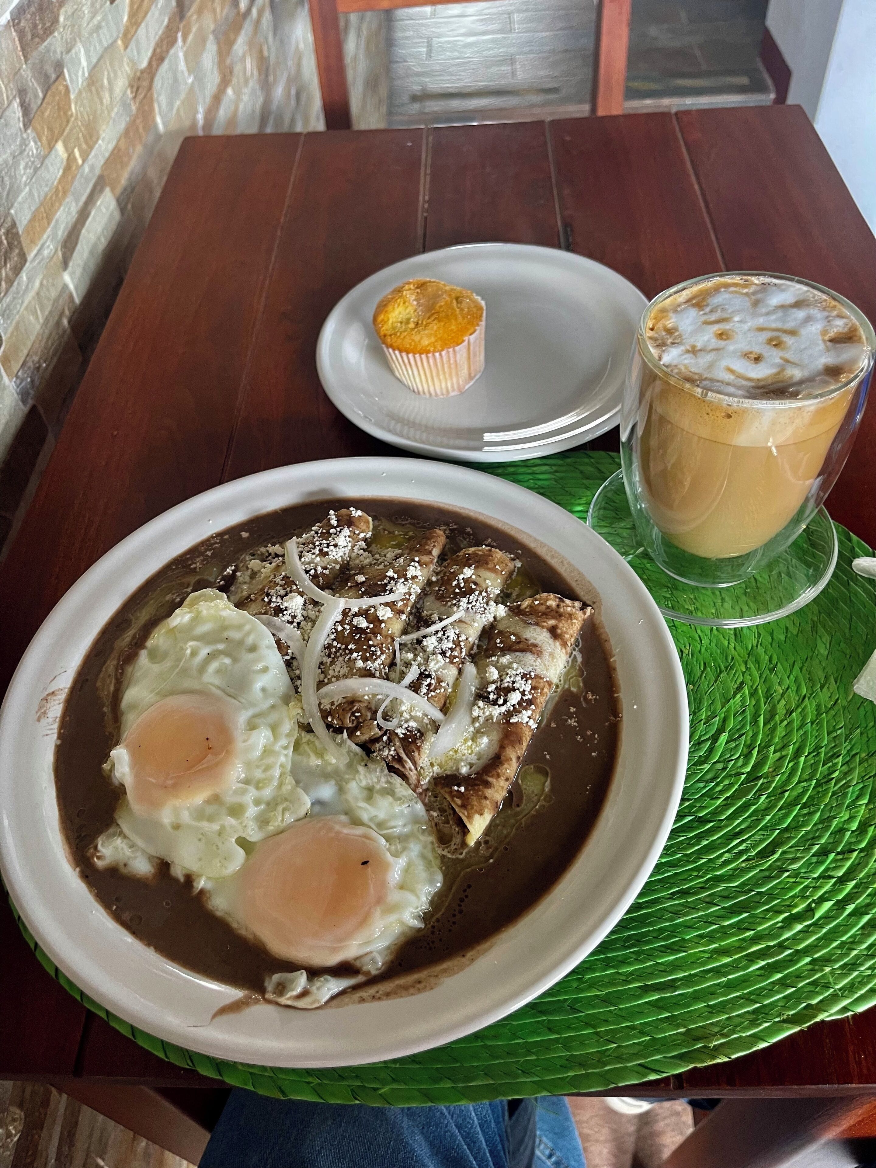 A table with a plate of food, a muffin, and a glass of iced coffee.