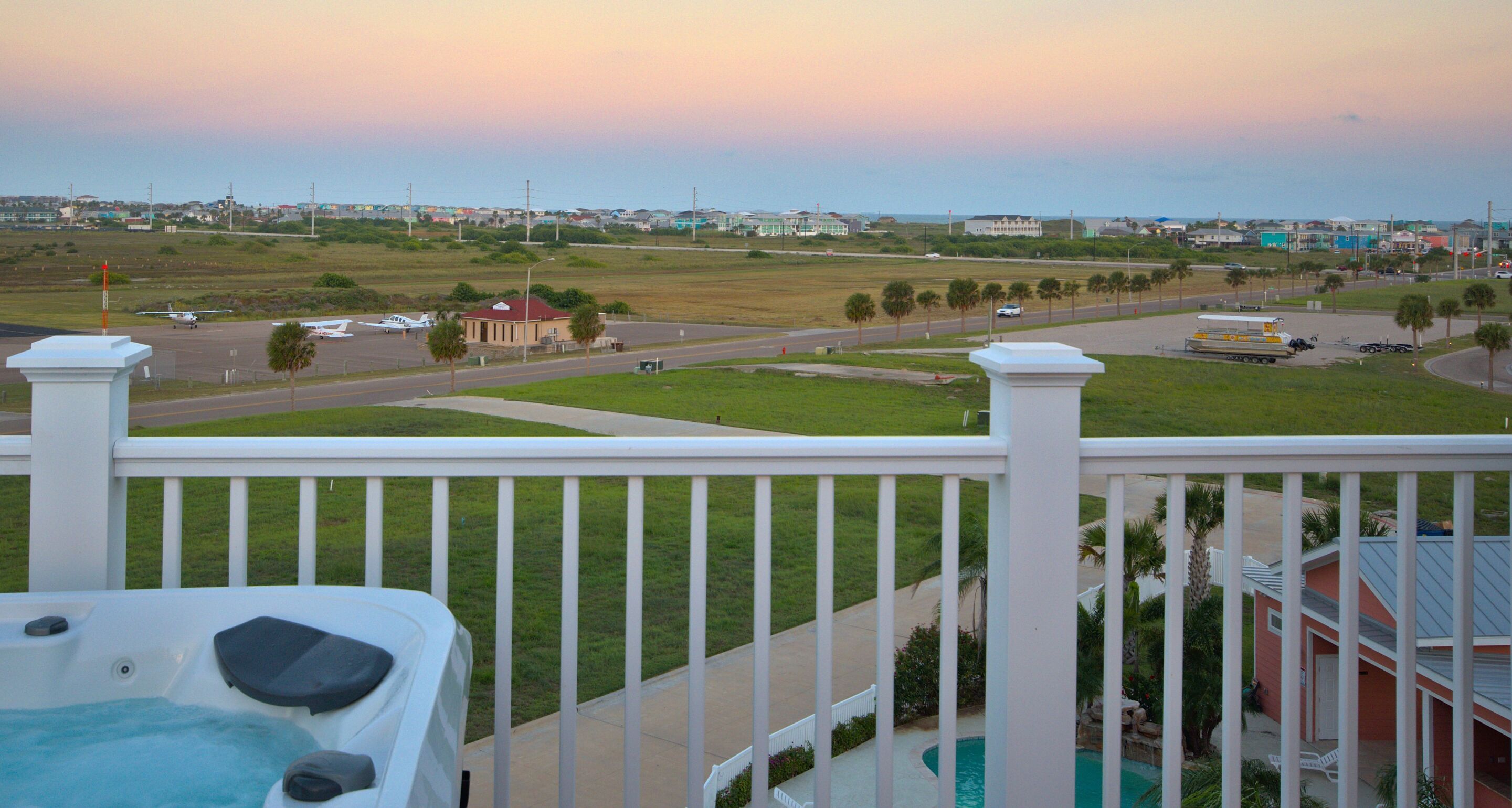 A balcony with a view of a grassy area, a road, and a building with a red roof.