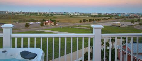 A balcony with a view of a grassy area, a road, and a building with a red roof.
