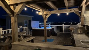 En udendørs terrasse med træbjælker, et boblebad og et grillområde.