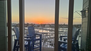 A view from a balcony with a wooden deck, featuring blue Adirondack chairs and a marina with boats.