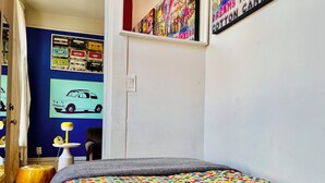 A bedroom with a colorful polka dot bedspread, a small table with a yellow lamp, and a wall with various posters and a car illustration. - FESTIVE GRAFITTI POP-ART 3BR - Wicker Park - Ukrainian Village (Chicago)