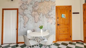 Une pièce avec un sol à carreaux, une table ronde entourée de chaises, une porte en bois portant un numéro et une carte du monde accrochée au mur.