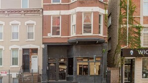 Une vue de rue avec une rangée de bâtiments, dont un immeuble d’angle avec une devanture noire et une enseigne sur laquelle on peut lire « WIC ».