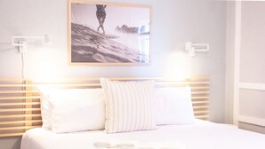 Ein ordentlich bezogenes Bett mit weißen Leinen und Kissen, ein gerahmtes Foto darüber und ein Stapel gefalteter Handtücher auf dem Bett.