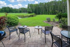 A patio with outdoor seating and a view of a golf course and forest.