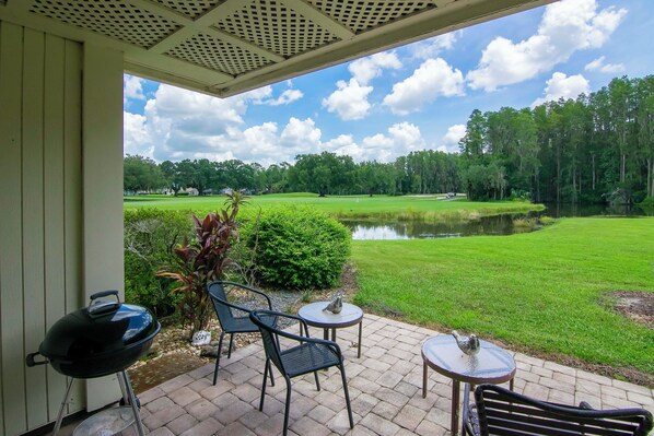 A patio with outdoor furniture, a grill, and a view of a golf course and pond. - First Floor 2bd/2ba Fully Remodeled Condo in Saddlebrook (Wesley Chapel)