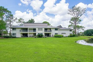 A two-story building with a flat roof, a covered patio area, and a small pond in the foreground. - Saddlebrook 1st Floor 2 bd/2 ba Fully Remodeled (Wesley Chapel)