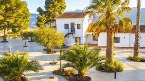 A white building with a red-tiled roof, surrounded by palm trees and other greenery, with mountains in the background. - El Refugio de El Espilo in Almería (Andalusia) (Lúcar)