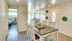 A dining area with a wooden table, white chairs, and a kitchen in the background. - Grand Junction Vacation Rental w/ Patio & Grill! (Grand Junction)