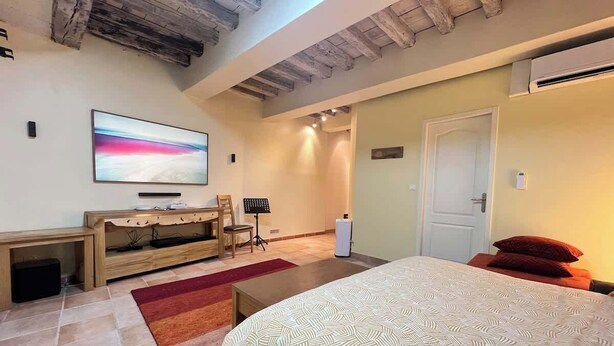 A bedroom with a large bed, a TV on a wooden stand, a desk with a chair, and a door.