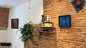 A room with exposed brick walls, a hanging plant, a geometric shelf with books, and two framed artworks.