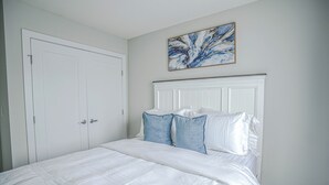 A bedroom with a white bed, white headboard, and a painting on the wall. - Peace Fort (Fort Saskatchewan)