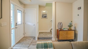 A hallway with a carpeted floor, a door, a staircase, and a small console table with a vase and a book. - Peace Fort (Fort Saskatchewan)