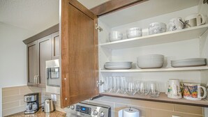 A kitchen with a stove, coffee maker, and shelves with dishes and glasses. - Peace Fort (Fort Saskatchewan)