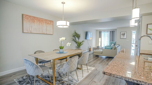 A modern kitchen with a granite countertop, a dining area with a wooden table and chairs, and a living area with a sofa and a TV. - Peace Fort (Fort Saskatchewan)