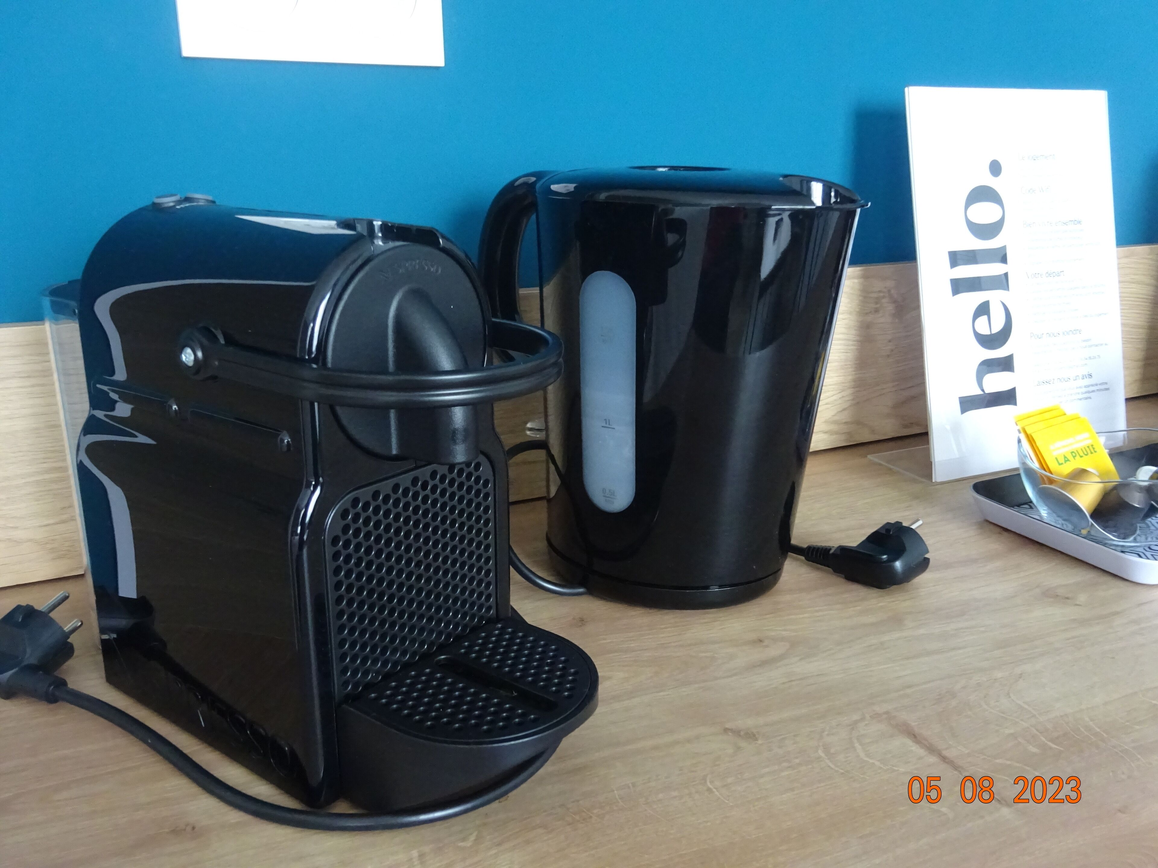 Een koffiezetapparaat, een prullenbak en een bordje met de tekst 'hello' op een houten tafel.