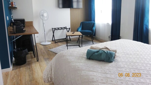 Une chambre d’hôtel équipée d’un lit, d’un bureau avec une imprimante, d’une chaise, d’un ventilateur sur pied et d’un téléviseur fixé au mur.