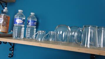 Una estantería con dos botellas de agua, un tarro de cristal y varios vasos.