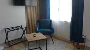 Un salon moderne avec un fauteuil bleu, une table basse en bois, un téléviseur noir fixé au mur et une fenêtre ornée de rideaux bleus.