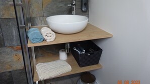 Une salle de bain avec un lavabo blanc, un porte-serviettes avec des serviettes bleues et blanches, une boîte de rangement noire et un tapis de bain blanc.