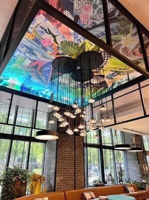 Ein modernes Interieur mit einer großen Wandmalerei, hängenden Lampen und bodengrossen Fenstern.