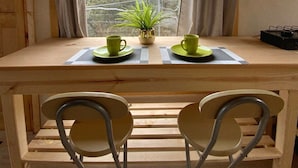 Un tavolo di legno con due sedie, una pianta in vaso e due tazze verdi su un sottopiatti a quadretti.
