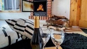 Una camera accogliente con camino, un letto con biancheria a righe, una bottiglia di vino e bicchieri su un tavolo.