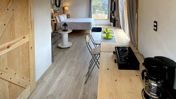 Una cucina compatta e moderna con travi in legno, zona pranzo con tavolo e sedie, un letto con comodino e un'ampia finestra.