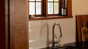 A kitchen with a window above the sink, a pendant light, and a bottle on the window sill. - At Leo's by Maison Dudley (Lac-Mégantic)