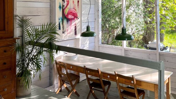 A rustic wooden interior with a dining table, chairs, a green pendant lamp, and a painting of a flamingo. - At Leo's by Maison Dudley (Lac-Mégantic)