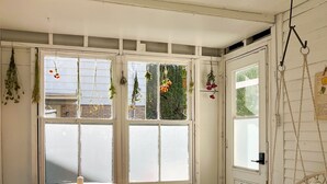 A room with a wooden table and chairs, a hanging chair, and a window with plants. - The Loft by Maison Dudley (Lac-Mégantic)