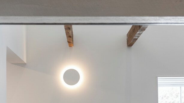 A staircase with a circular light fixture on the wall and a window with a view of trees. - The Loft by Maison Dudley (Lac-Mégantic)