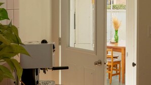 A kitchen with a coffee machine, a hanging light fixture, and a door leading to a dining area with a table and chairs. - The Loft by Maison Dudley (Lac-Mégantic)