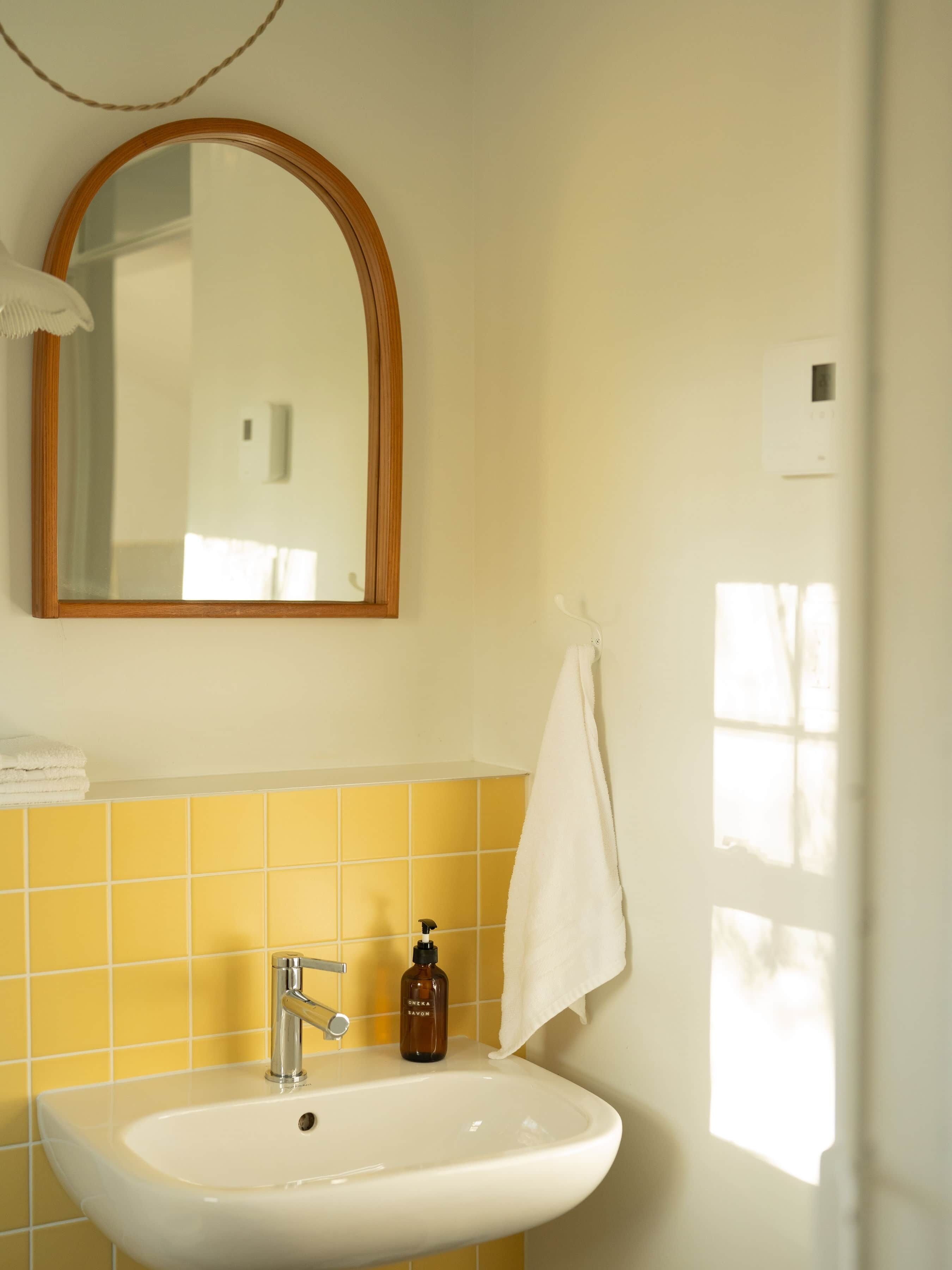 Ein Badezimmer mit einem weißen Waschbecken, gelben Fliesen, einem spiegel mit Holzrahmen und einem Handtuch an der Wand.