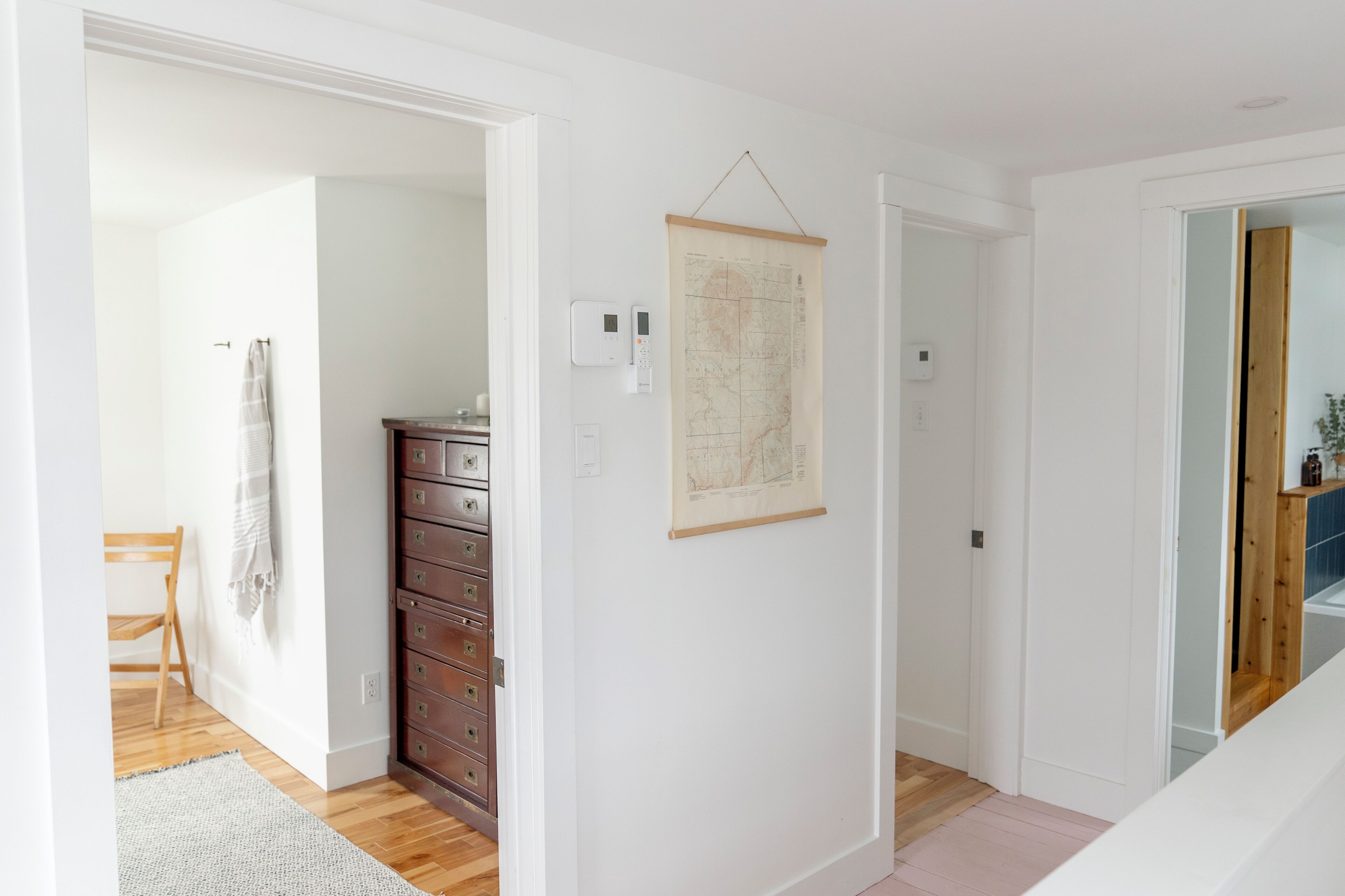 A hallway with a wooden dresser, a map on the wall, and a door leading to another room.