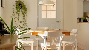 A dining area with a wooden table and white chairs, a hanging plant, and a pendant light above the table. - The Boulevard by Dudley House (Lac-Mégantic)