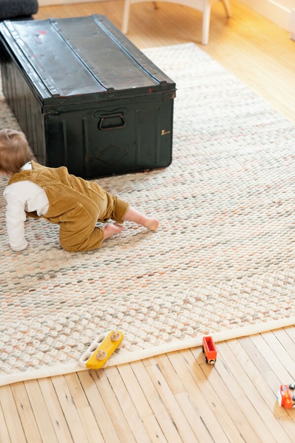 A child playing on a textured rug with toys and a large black suitcase in the background.