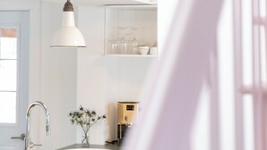 A modern kitchen with a white sink, a hanging pendant light, and a door leading to another room. - The Boulevard by Dudley House (Lac-Mégantic)
