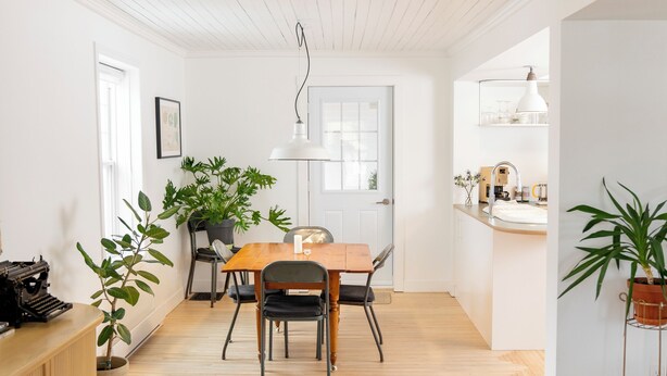 A modern living room with a wooden floor, a black sofa, a dining table with chairs, and a kitchen area with a sink and countertop. - The Boulevard by Dudley House (Lac-Mégantic)