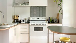 A modern kitchen with white cabinetry, a stainless steel sink, and a wooden floor. - The Boulevard by Dudley House (Lac-Mégantic)