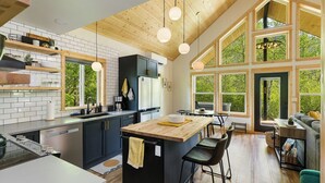 Une cuisine moderne dotée d’un grand îlot central, d’un plafond en bois et de grandes fenêtres offrant une vue sur la verdure.