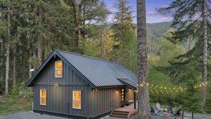 Une cabane avec un toit en métal, une véranda et une allée gravillonnée.