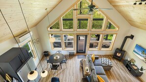 Un loft spacieux avec de hauts plafonds, de grandes fenêtres, un espace salon central comprenant un canapé et une table à manger, un poêle intégré et une cuisine équipée d’appareils électroménagers modernes.