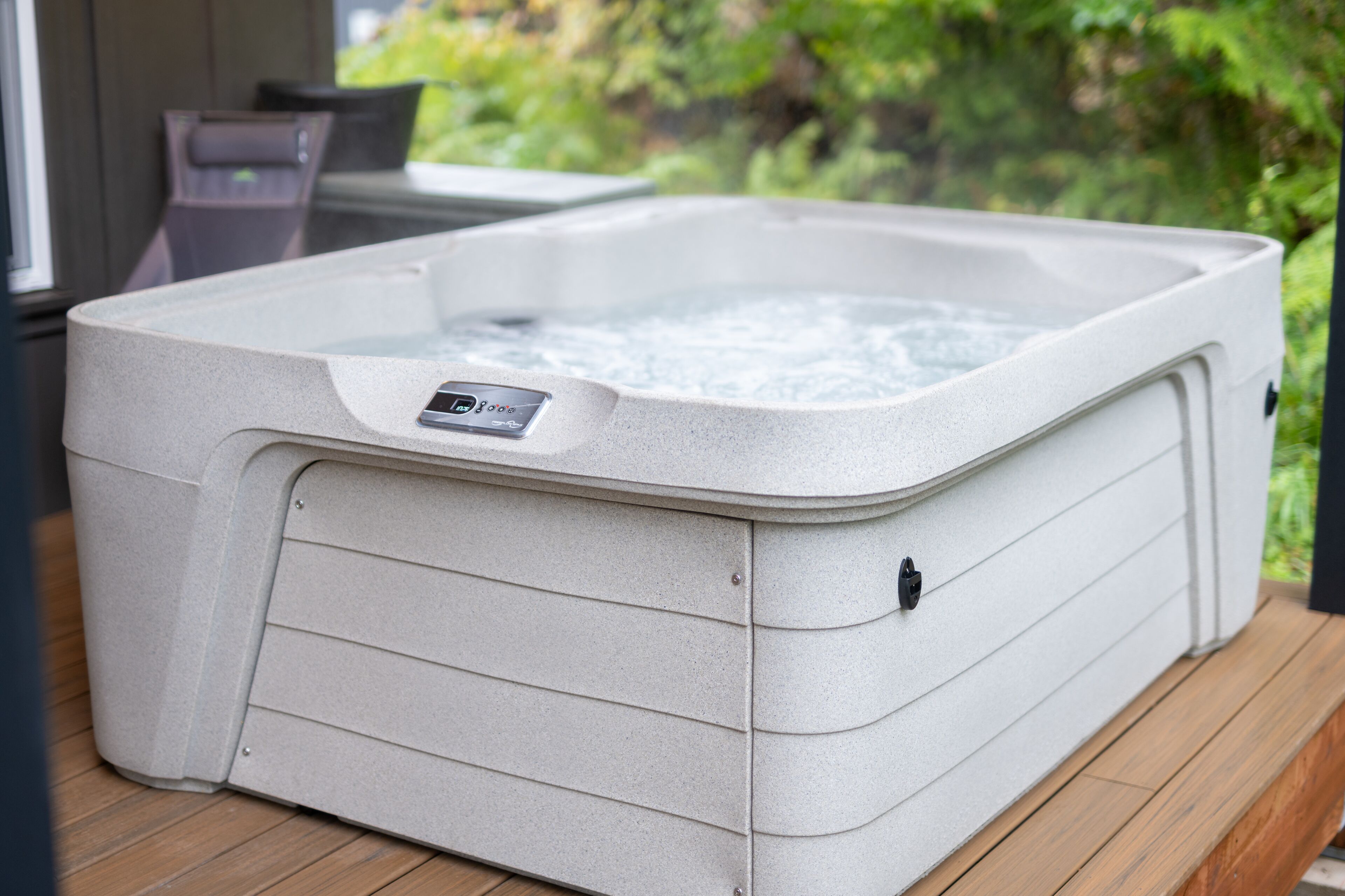 A spa hot tub with a control panel, set on a wooden deck with a view of greenery.