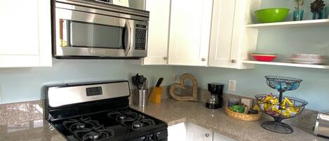 A modern kitchen with white cabinets, a stainless steel stove, a microwave, and a wooden ceiling vent.